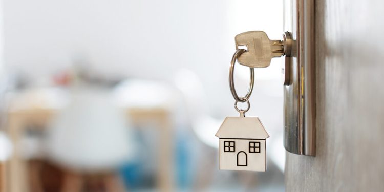 Key with keychain in a house shape in the door keyhole. Buy new home concept. Real estate market.