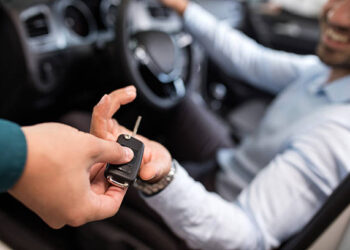 Close up of a man sitting in a car and receiving car keys from unrecognizable person.