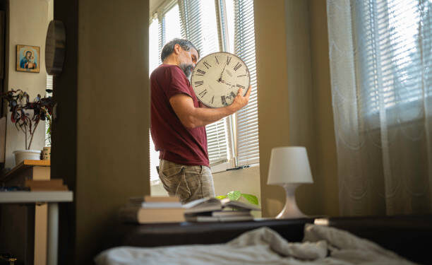 Mature man over 50s arranging his wall clock, changing the batteries at home. The single lifestyle concept.