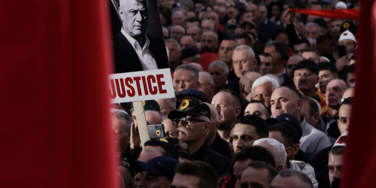A man holds a banner depicting former Kosovo President Hashim in Skanderbeg square central Tirana, Albania, Friday, Oct. 17, 2025, as people protest against war crimes trials being pursued against some of their leaders in The Hague. (AP Photo/Vlasov Sulaj)