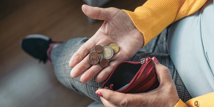 Close-up aerial image of a seated older woman's hand holding coins in her palm while holding a purse in her other hand.